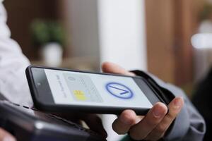 Close-up shot of tourist making contactless payment via mobile phone using NFC technology. Detailed view of pair of hands grasping pos terminal and smartphone, paying winter holiday reservation. photo