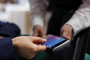 Close-up view of pair of hands grasping credit card and pos terminal at exclusive hotel reception. Detailed shot of person paying for reservation in lounge area of ski mountain resort. photo