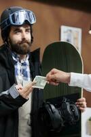 Detailed view of male snowboarder tipping employee with cash in ski hotel reception. Caucasian man in wintersport clothing giving gratuity to concierge at winter mountain resort. photo