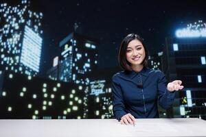 Presenter going live on transmission to open news segment for international television program, using headlines from media outlets. Asian reporter hosting night show to talk about events. photo