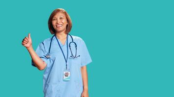 Cheerful experienced asian nurse showing thumbs up signs while at work, isolated over studio background. Friendly smiling BIPOC healthcare professional doing approval gestures photo