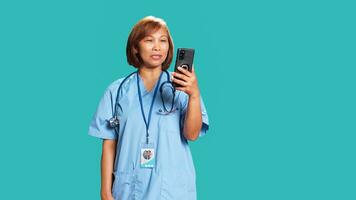 Happy nurse in videocall meeting over the phone, greeting people. Cheerful healthcare specialist in online telemedicine call with patients, isolated over blue studio background photo