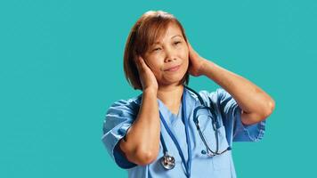 Competent nurse tormented by extreme noise while at work, close up. Healthcare employee covering ears with hands, bothered by rowdy surrounding sounds, isolated over studio background photo