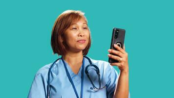 Close up shot of happy nurse in online videoconference meeting over the phone, greeting people. Joyful hospital employee in telehealth call with patients, isolated over studio background photo