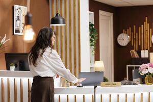 Retired senior woman arrives at front desk and rings the silver service bell for assistance from staff in hotel reception. Elderly female traveler waiting for customer service from resort employees. photo