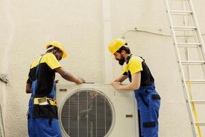 Expert master technician and apprentice serviceman dismantling old busted external air conditioner to replace it with new performant hvac system after draining refrigerant and replacing ductwork photo