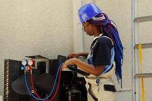 Electrician looking online for new evaporator coil after finding out of order condenser component during annual maintenance. African american expert checking air conditioner internal part stock photo