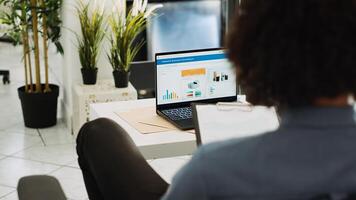 Middle eastern man studying trends and statistics to create annual report, using archives analytics. Business specialist examining online scoreboard with research data, coworking space. photo