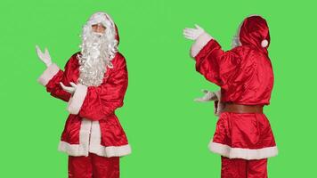 Man dressed like santa claus does ad in studio with greenscreen, wearing traditional december costume with white beard. Saint nick character showing advertisement, point aside. photo