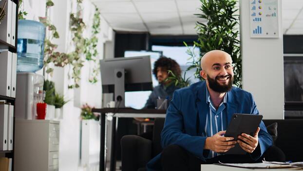 Employee comparing data on tablet while working in open space office. Unicorn business worker reviewing documents and annual statistics on device, trying to solve executive tasks. photo