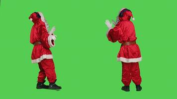 Santa claus using audio headset to listen to music and have fun during christmas eve holiday, full body greenscreen backdrop. Saint nick cosplay in costume dancing on songs, entertainment. photo