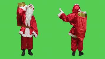 Papa Noel claus con rojo bolso dice Ho Ho Ho terminado lleno cuerpo pantalla verde fondo, vistiendo tradicional fiesta disfraz y lentes. padre Navidad cosplay que lleva saco con regalos y juguetes foto