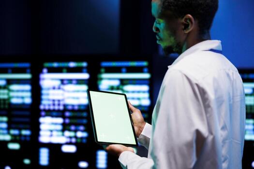 Technician utilizes green screen tablet to examine configuration settings of server clusters. Employee reviewing event logs in monitoring software to pinpoint root cause of faulty data center hardware photo
