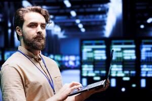 Expert IT programmer using laptop to assess supercomputer cybersecurity dangers arising due to unsecured network connections. Supervisor ensuring high tech facility is impenetrable by malware attacks photo
