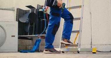 Meticulous mechanic in professional uniform with technical equipment climbing folding ladder to do maintenance on rooftop hvac system. Professional worker commissioned to check up on air conditioner photo