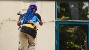 Adept repairman holding electric drill, stepping down from folding ladder after finishing check up on rooftop hvac system. Proficient worker at the end of maintenance assignment photo