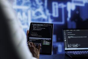 Admin updates neural networks made up of interconnected nodes, writing intricate binary code scripts on tablet and laptop, close up. Data center expert uses programming to upgrade AI simulation model photo