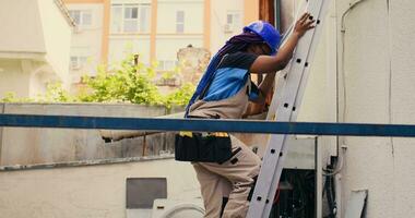 Proficient expert holding electric power drill stepping down from folding ladder after finishing servicing rooftop hvac system. Knowledgeable professional commissioned to checkup on air conditioner photo