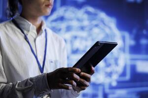 Admin using tablet in server room to maintenance artificial intelligence neural networks simulating human thought processes. High tech establishment worker does checkup on AI systems photo