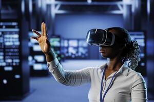 Computer scientist in data center uses virtual reality to prevent system overload. African american VR headset user in server room ensuring enough network bandwidth for smooth operations photo