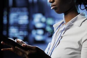 Focused admin in data center uses tablet to prevent server machines overload. Expert between server mainframes using device to ensure enough network bandwidth for smooth operations photo