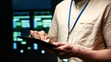 Meticulous technician doing checkup, inputing data on tablet of needed fixes in server hub housing advanced data storage infrastructure supporting critical IT workloads, close up photo