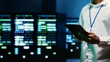 IT specialist walking through server rows performing data backups, close up. Serviceman using tablet to make sure electric generators are able to ensure operational continuity photo