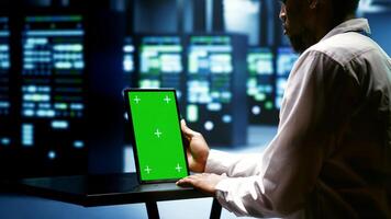 Specialist using green screen tablet to check server rigs doing intense computations. Technician preventing strain on data center equipment caused by AI applications driving up power usage photo