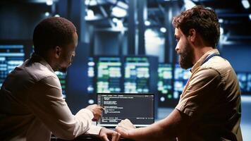 IT developers team writing server script code in data center on laptop terminal. Teamworking programmers doing maintenance work in high tech facility updating rigs software photo