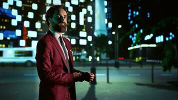 Businessman walking at night in the city, enjoying late stroll in the dark with skyscrapers and illuminated sidewalk. Person in suit looking at urban buildings and streetlamps, downtown district. photo