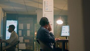 African american businessman enjoying music while checking statistical graphs on computer. Relaxed employee with headphones on solving project tasks in office during nightshift photo