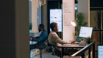 African american supervisor asking accountant to show him business project tasks progress in modern office during nightshift. Management executive overseeing employee working on computer photo