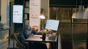 Coworker leaving work, dissaproving of employee falling asleep in desk chair overnight. Businessman finishing nightshift, dissapointed to see colleague sleeping at computer in office photo