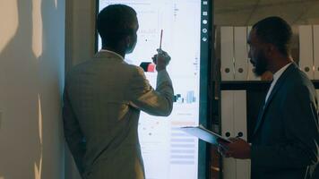 Supervisor showing employee useful datasets on digital screen to help him finish project tasks. Business executives looking over accounting figures in office during nightshift photo