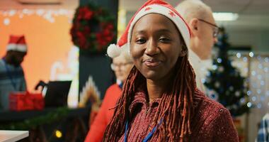 Portrait of smiling employee wearing Santa hat walking through clothing rack rows in xmas adorn shopping mall store, using clipboard to crosscheck price tags, making sure shop is ready for customers photo