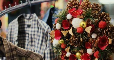 Dolly out shot of festive Christmas wreath decorated with pine cones hanging from clothes rack in empty shopping mall store, ready to bring holiday cheer during winter holiday season, close up photo