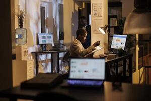 Corporate worker checking financial report on computer working at company statistics late at night in startup office. Businessman typing marketing strategy, planning profit progress photo