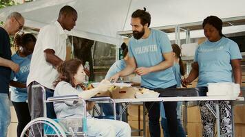 Helpful guy volunteer offers free lunch to the poor disabled woman in need. Multiracial charity workers at an outdoor food bank provide the handicapped and less fortunate with hunger relief. photo