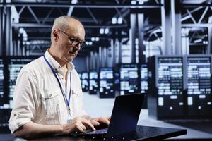 Experienced serviceman using laptop, setting up high bandwidth dedicated multiplayer gaming servers in high tech establishment to accommodate more traffic from worldwide locations and avoid low ping photo