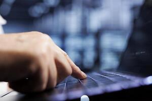 Cloud computing company executive using laptop to examine server racks for power fluctuations, close up. Trained employee monitoring high tech data center rigs parts, identifying potential errors photo