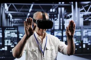 Elderly adept technician immersed in virtual reality at data center, doing infrastructure maintenance. Specialist using VR headset to optimize server clusters system performance photo