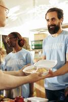 A diverse group provides humanitarian aid at a community center, distributing free food to the homeless. Multiracial volunteers collaborate to support the underprivileged and organize food drives. photo