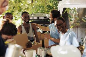 African American woman and caucasian man smile while providing boxes of canned goods handing out donation boxes to needy. Individuals volunteering by sharing necessities to poor and homeless people. photo
