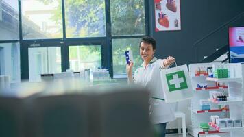 Portrait of happy pharmacist in apothecary excited to provide pharmaceutical products to clients. Joyful healthcare expert holding prescription pills box and shopping bag in drugstore photo