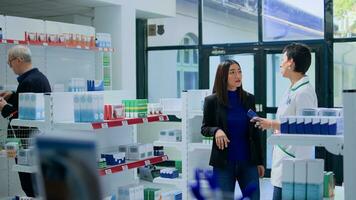 Asian woman in drugstore asking qualified pharmacist for medical recommendation. Licensed druggist helping customer pick best pharmaceutical product to counteract illness photo