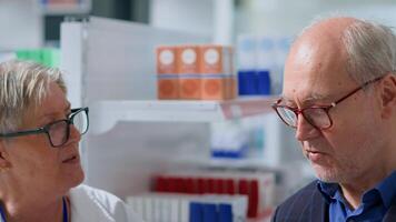 Aged pharmacist in apothecary using electronic thermometer on older man, checking temperature. Patient and healthcare professional during routine consultation, monitoring flu symptoms such as fever photo