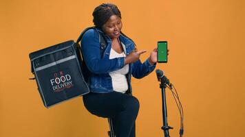 Young black woman showcasing reliable and efficient mobile app on device with blank chromakey copyspace template. Technology-driven delivery person grasping smartphone with green screen display. photo