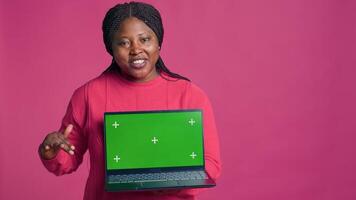 Young lady with african american ethnicity grasping laptop showcasing isolated chromakey template. Minicomputer with mockup green screen display held by beautiful black woman. photo