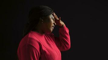 Black woman suffering from terrible headache displaying exhaustion and unpleasant response in isolated background. Side-view portrait of young female with migraine stroking temples to relieve tension. photo