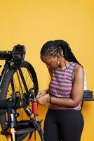 africano americano hembra ciclista ajusta y refacción bicicleta componentes con especializado caja de herramientas, asegurando óptimo actuación. deportivo negro mujer utilizando llave inglesa a para bicicleta rueda ajustamiento. foto